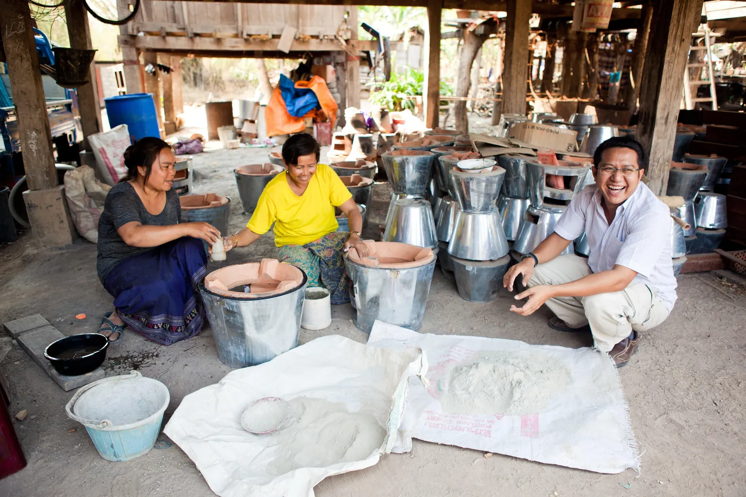 Three people sitting in a rustic workshop, manufacturing improved cookstoves